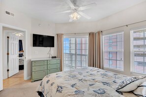 Un dormitorio con cama, ventilador de techo, televisión, cómoda y balcón con vistas.