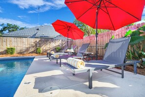 A poolside area with lounge chairs and red umbrellas, a wooden fence, and a metal roof. - Excellent Village Location | Private Pool | EV Charger | Dog Friendly! (Saint Simons Island)