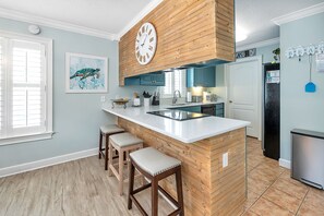 A kitchen with a wooden island, bar stools, a clock, and a refrigerator. - Excellent Village Location | Private Pool | EV Charger | Dog Friendly! (Saint Simons Island)
