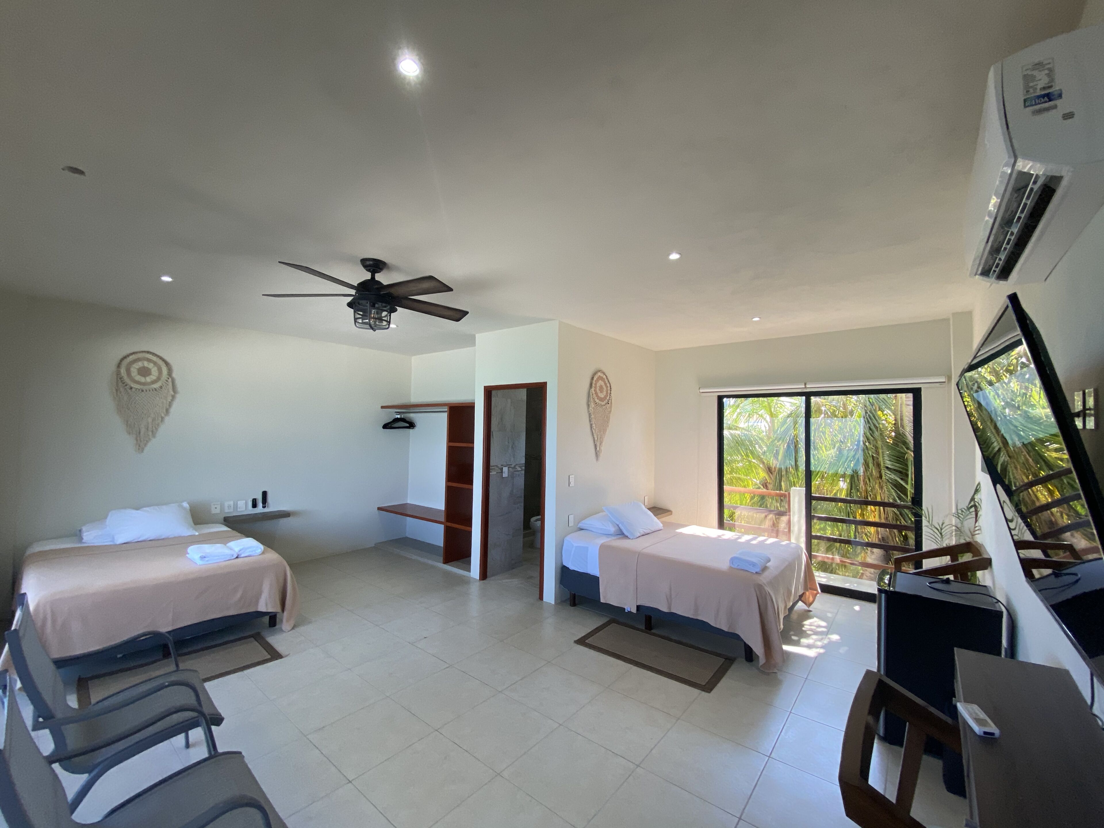 A hotel room with two beds, a ceiling fan, a TV, and a large window with a view of palm trees.
