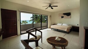 Un dormitorio con cama, ventilador de techo, ventana grande y vista al océano.