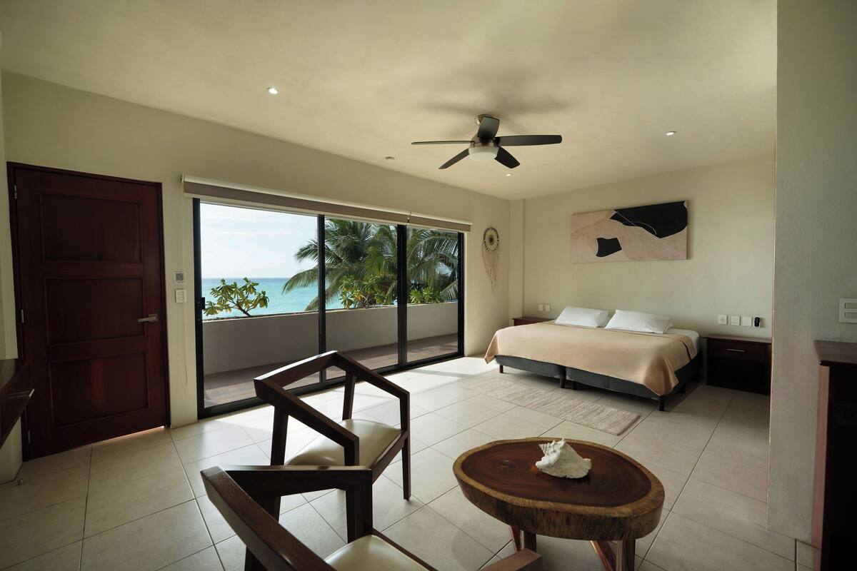 Un dormitorio con cama, ventilador de techo, ventana grande y vista al océano.