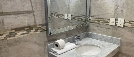 Une salle de bain avec un lavabo en marbre, un miroir et un distributeur de serviettes.