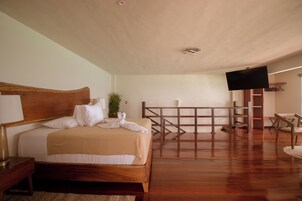 Una habitación de hotel con una cama de madera, un televisor montado en la pared y suelo de madera.