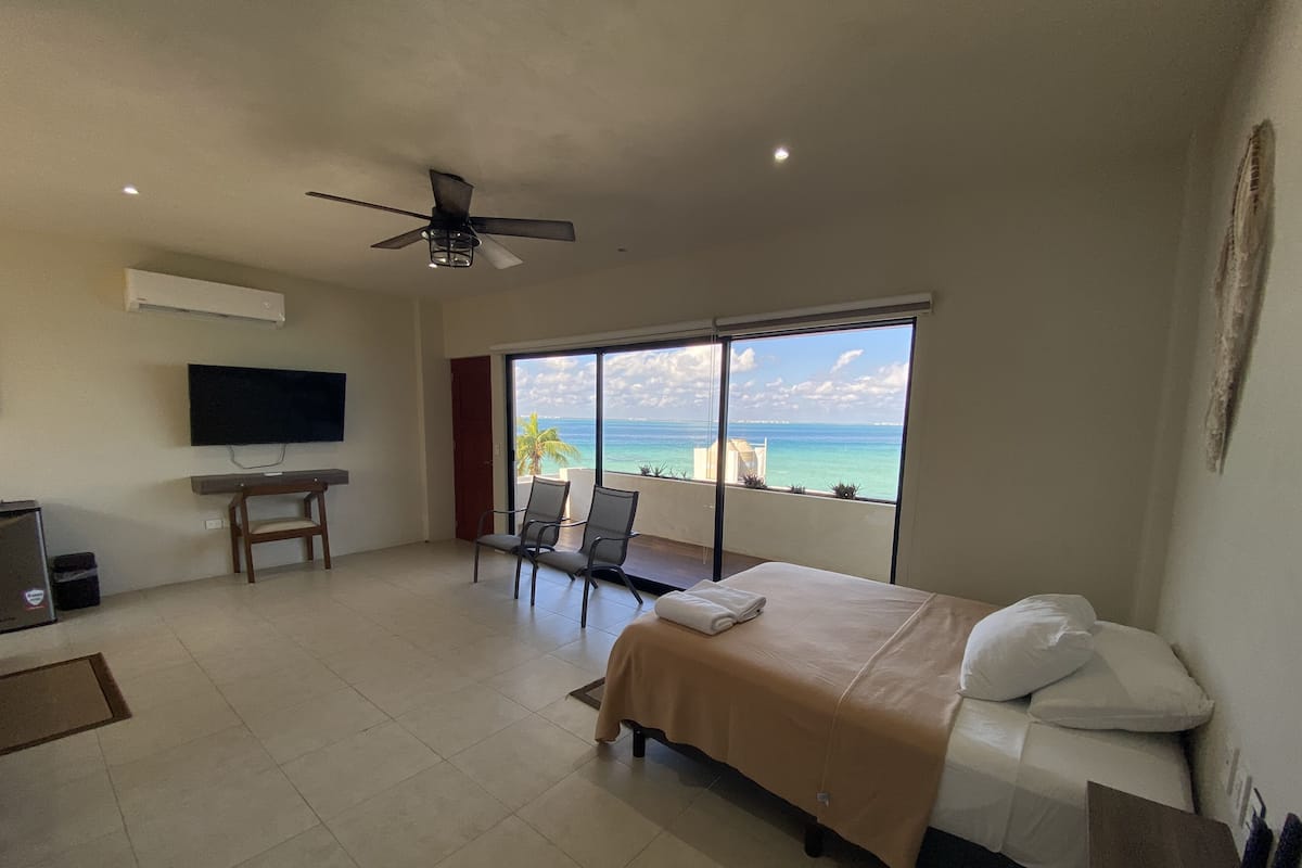 Habitación de hotel con cama, escritorio, televisor y balcón con vista al océano.