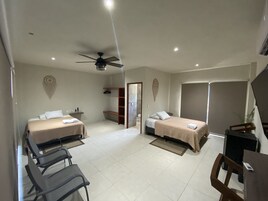 Una habitación de hotel con dos camas, un escritorio, una silla, un ventilador de techo y un baño pequeño.
