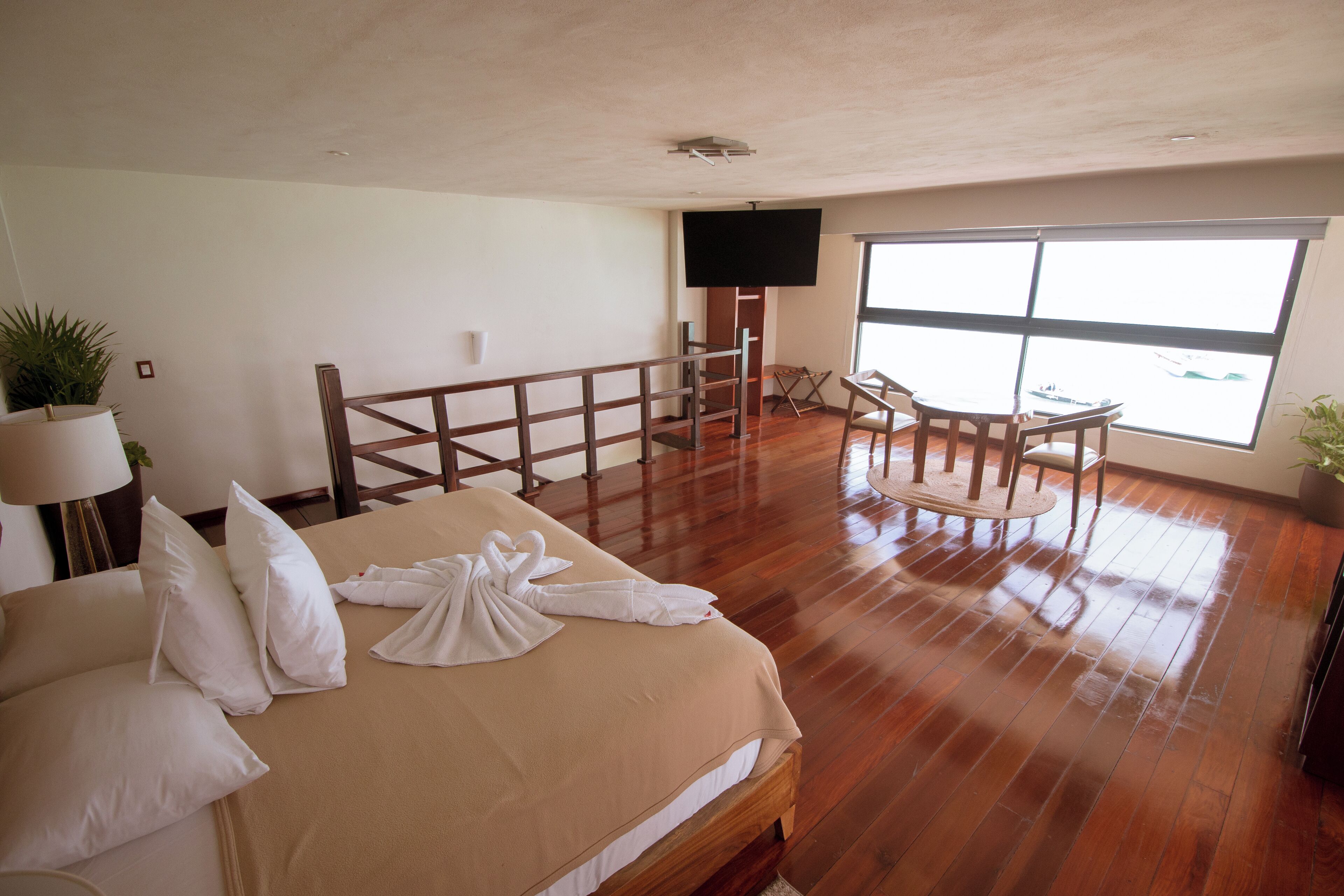 Une chambre d’hôtel avec un grand lit, une télévision, un balcon avec une chaise et une vue sur la mer.
