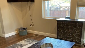 Um quarto com uma mesa de madeira escura, uma bandeja de metal, uma televisão na parede, uma janela com persianas e uma lareira de pedra.