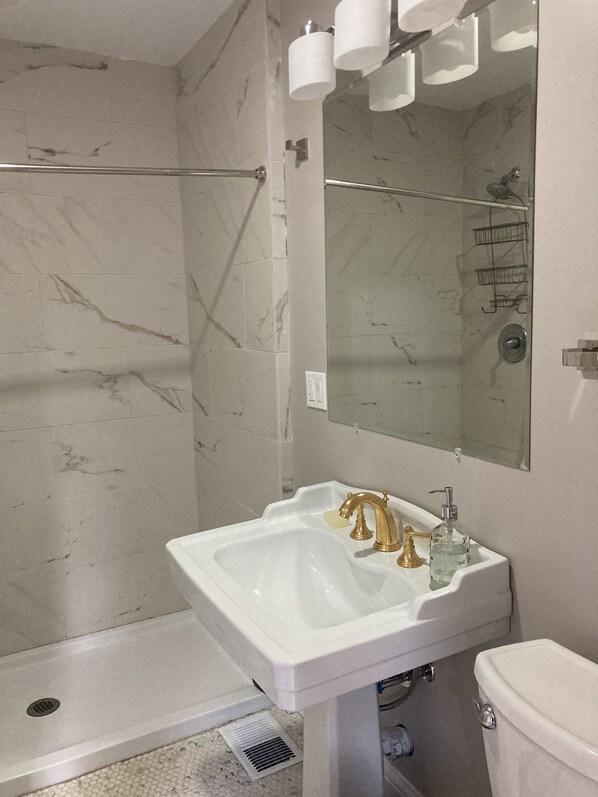A bathroom with a white sink, gold faucets, a mirror, and a shower area.