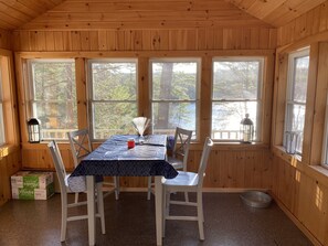 Una cabaña de madera con una mesa de comedor y sillas, ventanas amplias y vistas a árboles.