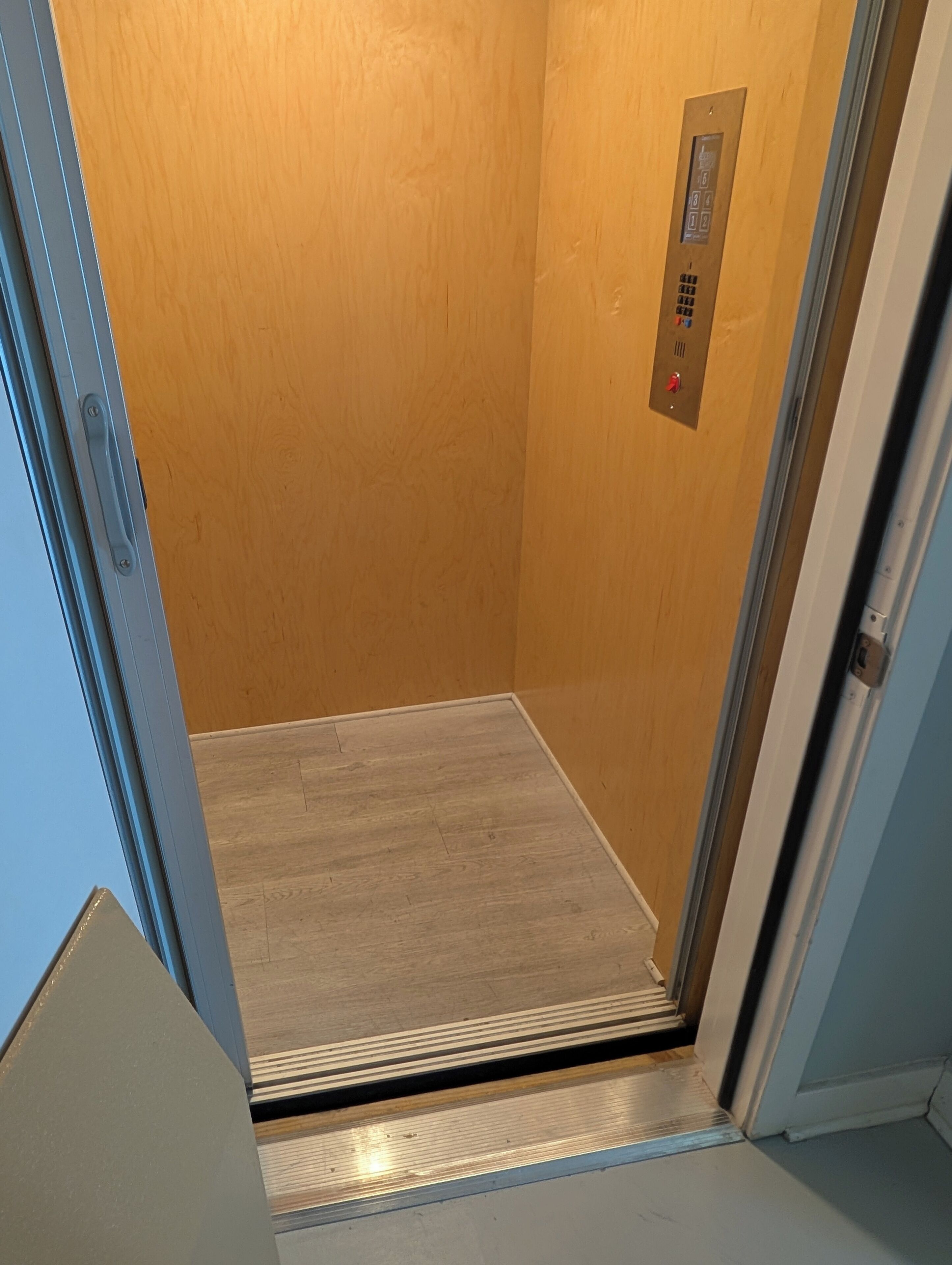 An elevator with a wooden wall and a metallic floor.