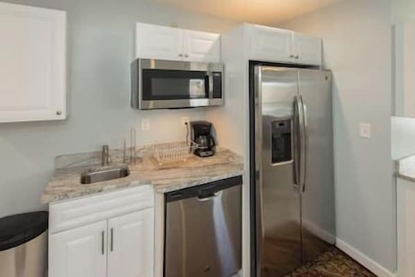 A compact kitchen with white cabinets, a stainless steel refrigerator, a microwave, and a coffee maker on the countertop.
