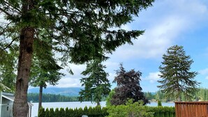 A lakeside patio with a wooden bench, picnic table, and a view of a lake and mountains. - Lake Nahwatzel Resort, Cabin #1, Shared Dock just steps away! Now with WIFI! (Shelton)