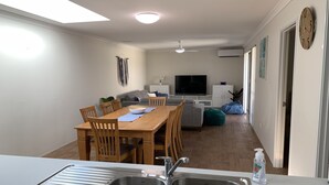 A modern kitchen with a double sink, dining area with wooden chairs, a TV, and a sofa. - Skylight Retreat Falcon (Falcon)