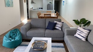 A modern living room with a grey sofa, teal bean bag, and a coffee table with a book and decorative items. - Skylight Retreat Falcon (Falcon)