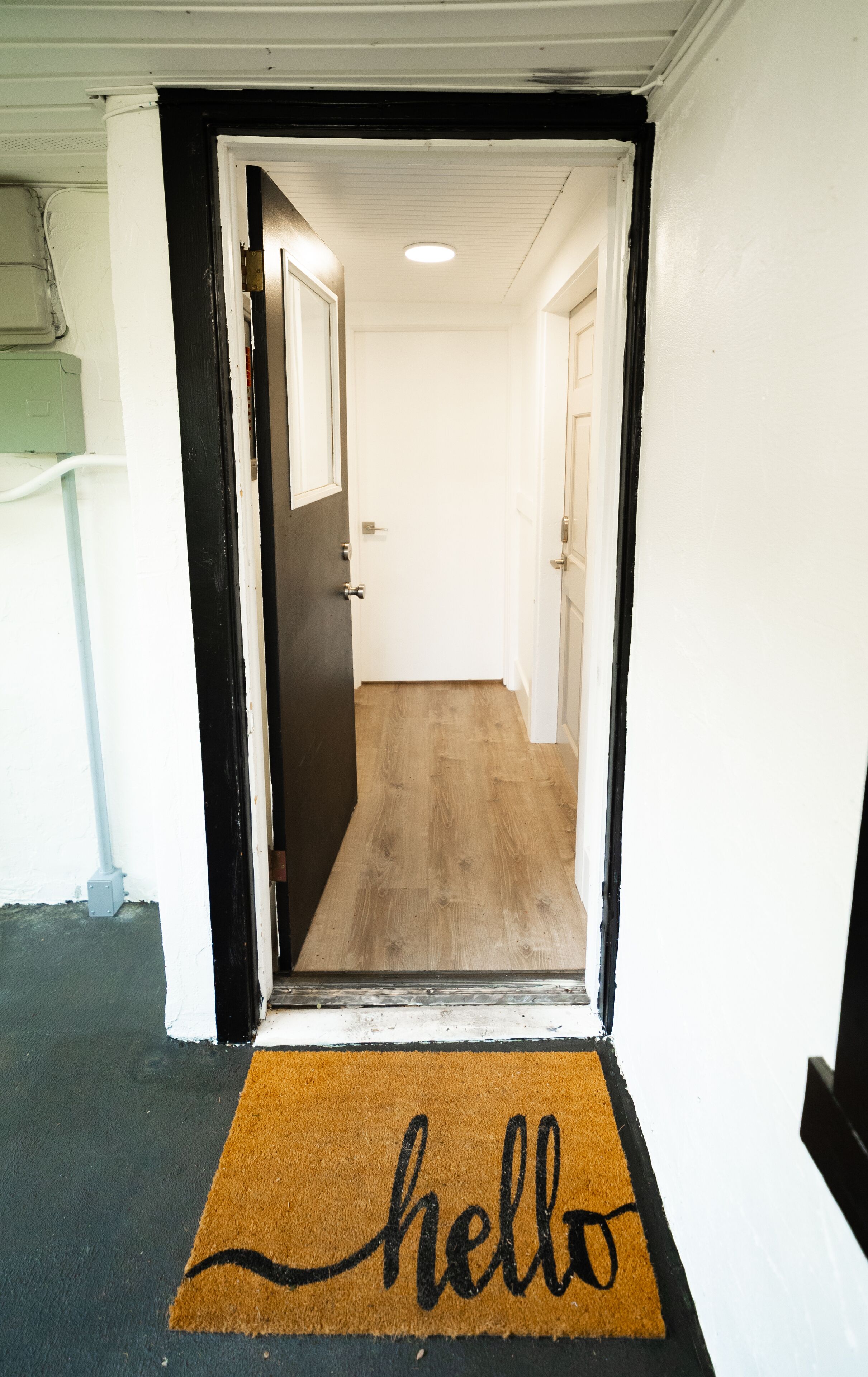 Un couloir doté d’un plancher en bois, de murs blancs et d’un chambranle de porte noir.