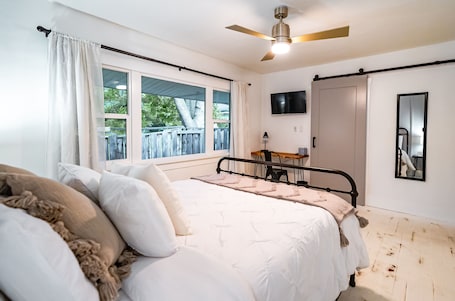 A bedroom with a bed, a ceiling fan, a TV, and a window with a view of a deck.