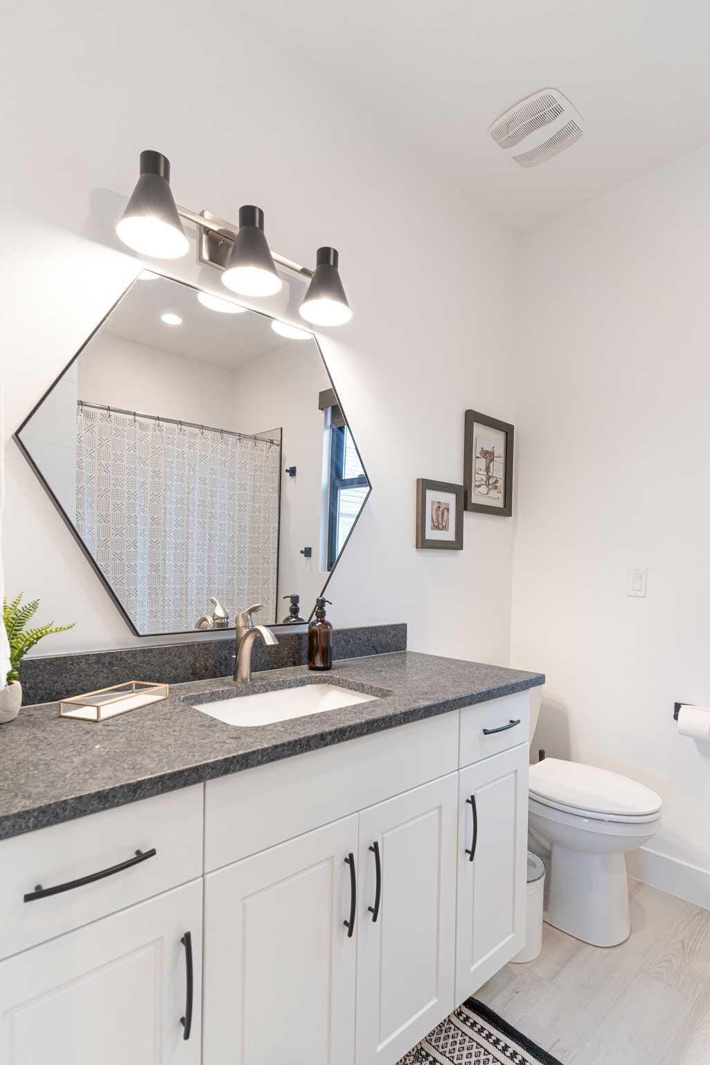 A modern bathroom with a large mirror, two sinks, a toilet, and a shower.