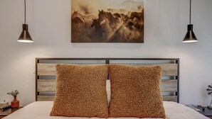 A bedroom with a wooden headboard, two fluffy pillows, a painting of horses, and pendant lights. - Modern | Clean | Getaway for Two! Mini Ranch Casita (Washington)