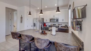 A modern kitchen with a central island, bar stools, pendant lighting, stainless steel appliances, and white cabinetry. - Modern | Clean | Getaway for Two! Mini Ranch Casita (Washington)