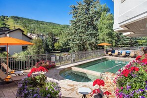 A swimming pool with a view of a forested hill, surrounded by lounge chairs and umbrellas.