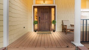 A wooden porch with a brown door, two potted plants, and a chair. - 1920's Sunny Gem - Downtown Waco Home (Waco)
