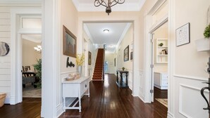 A hallway with wooden flooring, white walls, and a staircase leading to another level. - 1920's Sunny Gem - Downtown Waco Home (Waco)