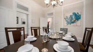 A dining room with a dark wooden table set for six, white plates, bowls, and a glass pitcher. There are six chairs around the table, and a chandelier hangs from the ceiling. - 1920's Sunny Gem - Downtown Waco Home (Waco)
