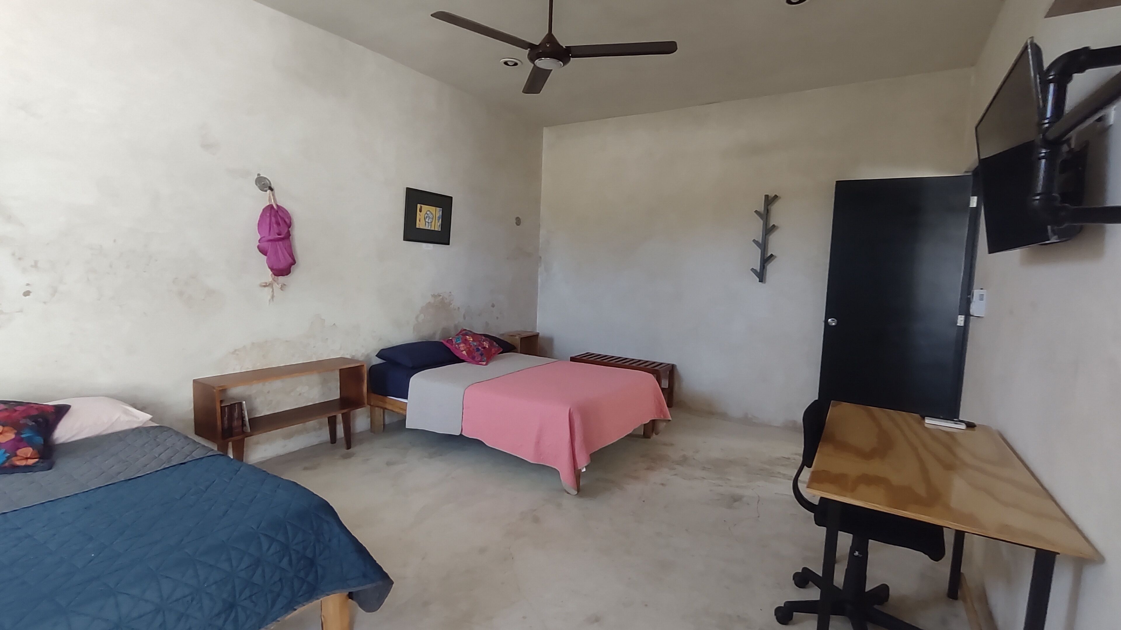 A room with three beds, a desk, a ceiling fan, and a TV mounted on the wall.