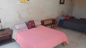 A bedroom with two beds, each with a different colored bedspread. There is a wooden nightstand with a lamp on the left side of the room.