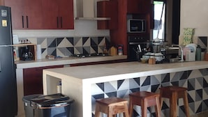 Una cocina moderna con una isla central, taburetes de madera, un cubo de basura y un microondas.