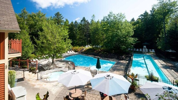 A backyard with a rectangular swimming pool, surrounded by lounge chairs and umbrellas.