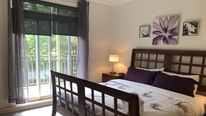A bedroom with a wooden bed, a nightstand, a lamp, and a window with curtains.