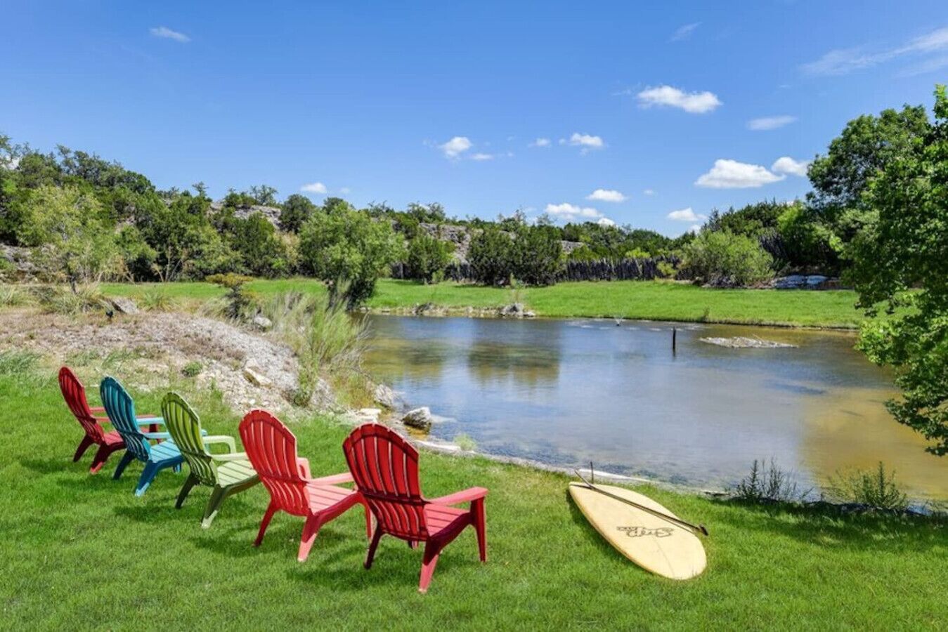 A grassy area with a pond, surrounded by trees and chairs.