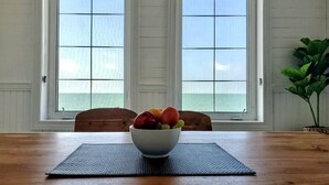 A dining table with a bowl of fruit in the center, two windows with a view of the ocean, and a potted plant to the right. - Newly Renovated! Paradise Point Lake House (Leamington)