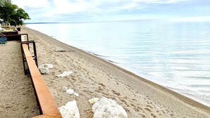 A beach with a wooden bench and a chair, a rocky area, and a clear view of the ocean. - Newly Renovated! Paradise Point Lake House (Leamington)