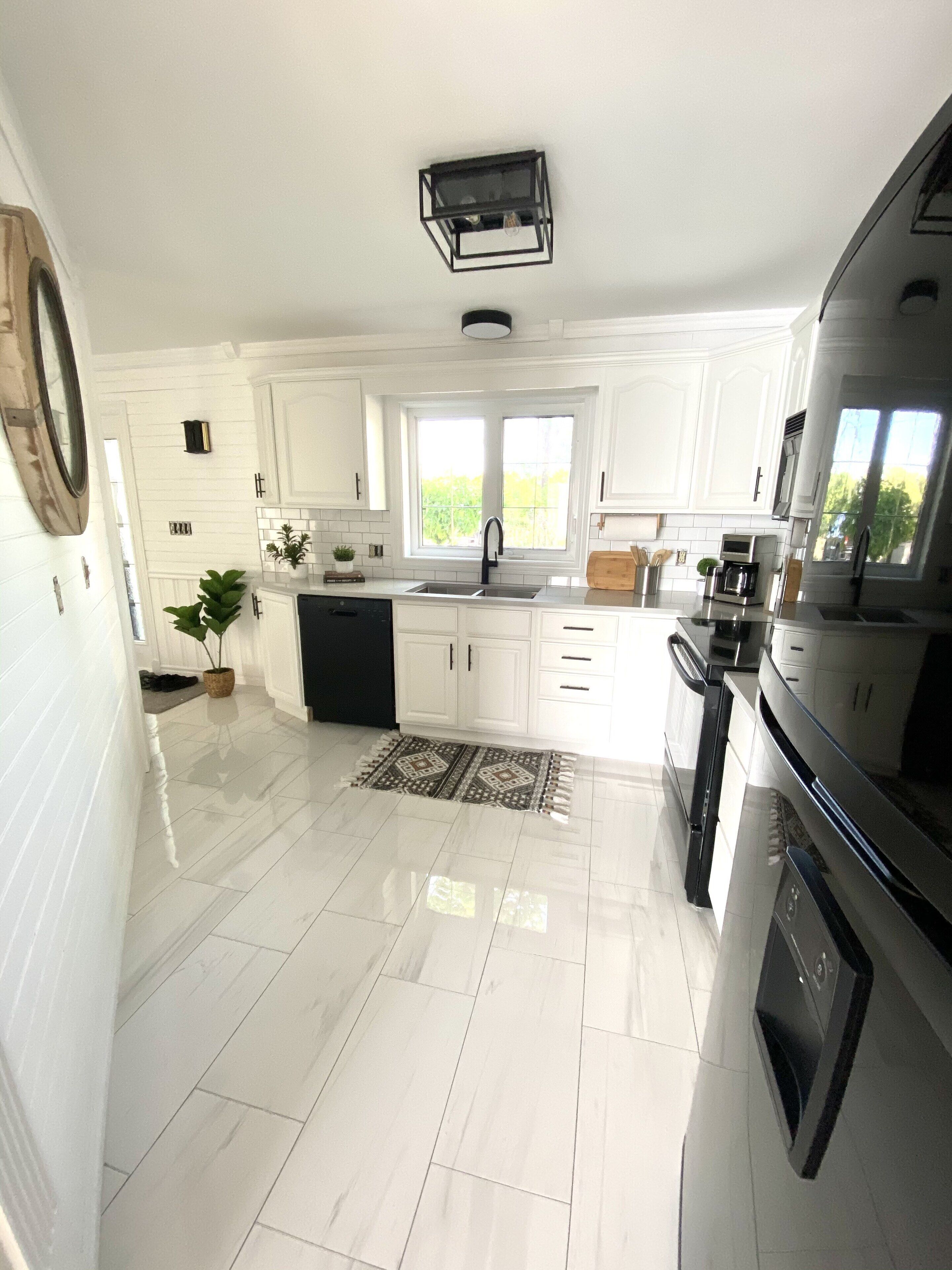 Une cuisine moderne avec des meubles blancs, une cuisinière noire et une fenêtre qui laisse entrer la lumière naturelle.