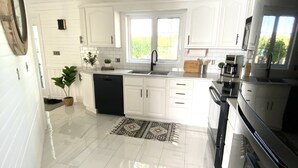 A modern kitchen with white cabinetry, a black stove, and a window providing natural light. - Newly Renovated! Paradise Point Lake House (Leamington)