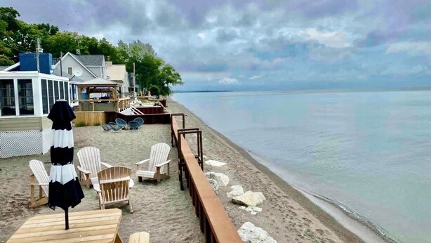 A beachside area with wooden chairs and tables, a wooden deck, and a view of the water. - Newly Renovated! Paradise Point Lake House (Leamington)