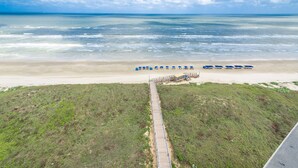 Een strand met een houten looppad dat uitkomt bij een rij blauwe parasols.