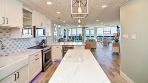 Een moderne keuken met witte kasten, een marmeren eiland en uitzicht op de woonkamer.