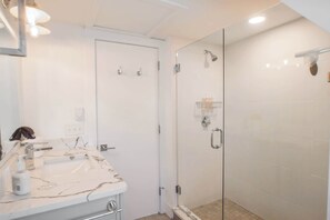 Une salle de bain avec un lavabo en marbre, une cabine de douche en verre et une porte blanche.