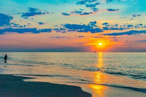 Solnedgang over et roligt hav med en person stående på stranden.