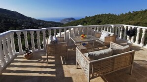 Un balcone con mobili in vimini, un tavolo con della frutta e vista sul mare e sulle colline.