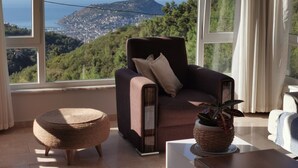 Una camera accogliente con un'ampia finestra che offre una vista panoramica su una città costiera e delle colline.