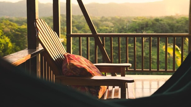 Una terraza de madera con una silla y una mesa, con vistas a un paisaje verde exuberante y montañas a lo lejos.