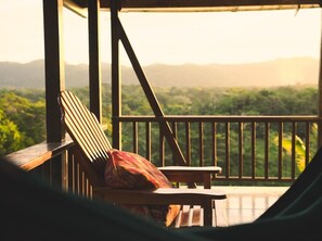 Una terraza de madera con una silla y una mesa, con vistas a un paisaje verde exuberante y montañas a lo lejos.