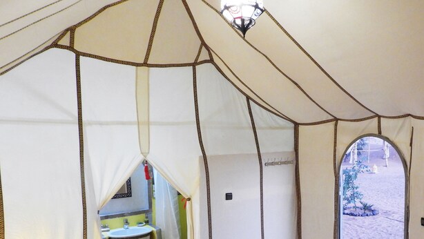 A tented room with a bed, a small table with a sink, and a view of the outside.