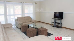 Ein Wohnzimmer mit einem beigen Sofa, einem Glastisch und einem Flachbildfernseher auf einem Standfuß.