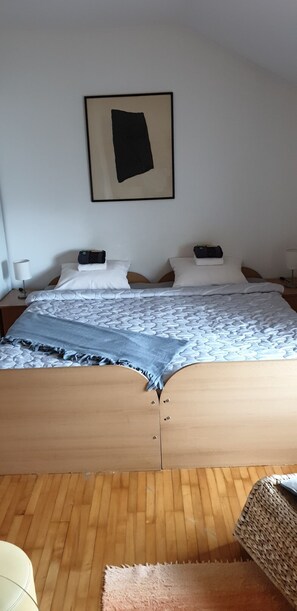 A bedroom with a wooden bed, white bedding, a black abstract painting on the wall, and a wooden floor.